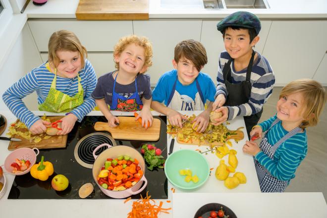 5 Kinder sitzen um einen Tisch und kochen